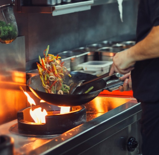 chef cooks vegetables in wok over flame